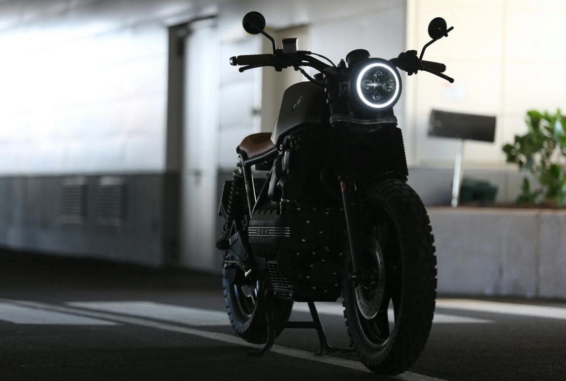 A custom BMW motorcycle with a circular LED headlight in a dimly lit parking area.